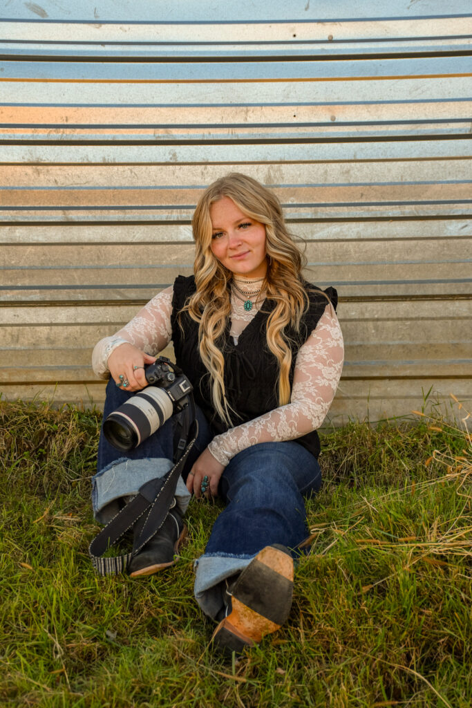 Woman sitting down holding a camera, smiling outdoors